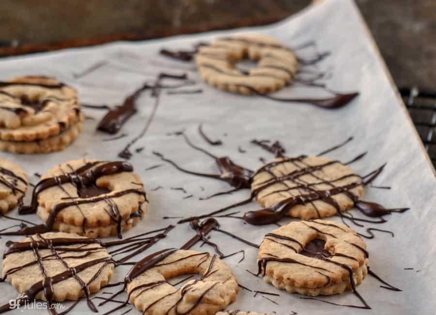 gluten free chocolate linzer cookies on tray with melted chocolate