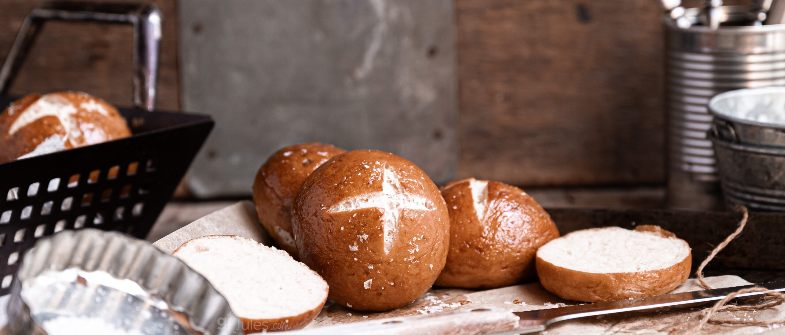 Golden-brown gluten free pretzel rolls cooling on a baking tray, sprinkled with coarse salt